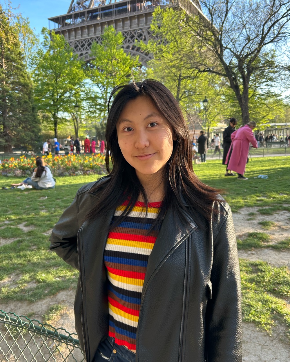 Emily Fang in Paris, smiling, wearing a black leather jacket and a striped top